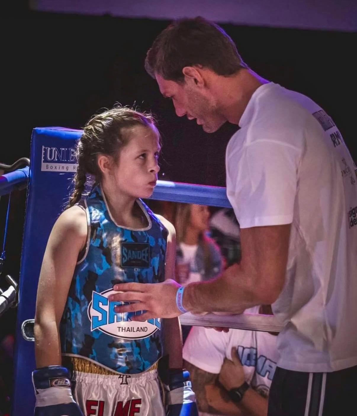 Liam Nolan coaching a young fighter ringside at a Muay Thai competition